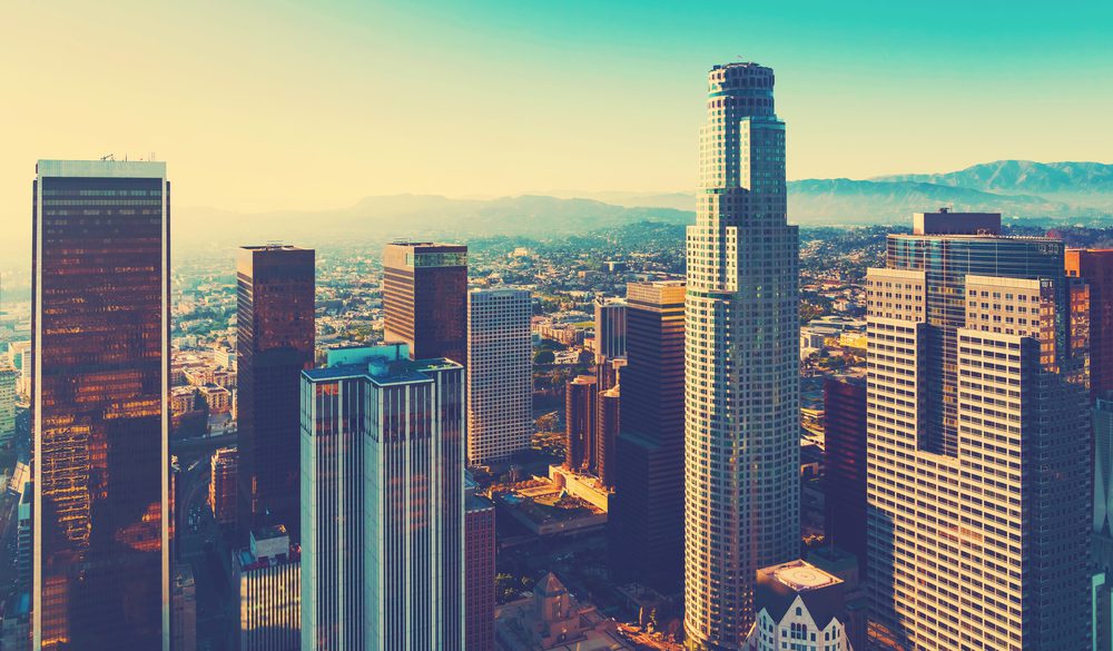 Aerial view of downtown Los Angeles skyscrapers bathed in warm sunlight, with mountains in the background under a clear blue sky—capturing the vibrant energy that inspires top Los Angeles Printing Solutions.