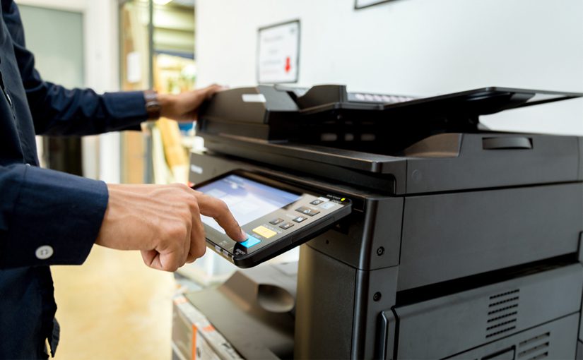 A person in a dark shirt uses the touchscreen panel on a black printer in an office setting, following a Basic Guide for Managed Print Services.
