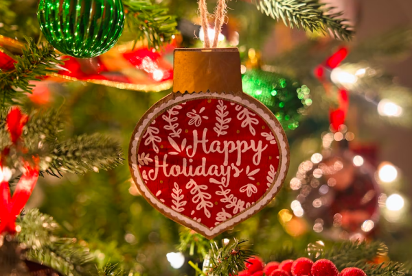 A red and white ornament on a Christmas tree reads Happy Holidays, surrounded by green branches, twinkling lights, shiny GoodSuite baubles, and festive decorations.